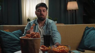 Abur cubur reklamı konsepti. Adam evde fast food dağıtımı ile vakit geçiriyor, kanepeye oturup televizyon izliyor, sosa batırılmış tavuk yiyor, kola içiyor, tadını çıkarıyor. Yavaş çekim