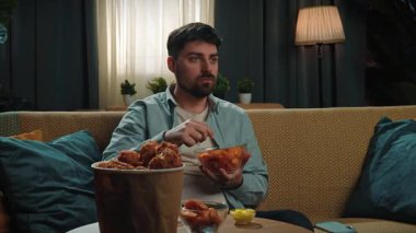 Abur cubur reklamı konsepti. Sakallı adam evde fast food dağıtımı ile vakit geçiriyor, kanepede oturup spor televizyon izliyor, takımı alkışlıyor ve cips yiyor, mutlu bir zafer ifadesi. Yavaş çekim