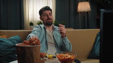 Abur cubur reklamı konsepti. Sakallı adam evde fast food dağıtımı ile vakit geçiriyor, kanepede oturup spor televizyon izliyor, ekranla konuşuyor ve soslu patates yiyor. Yavaş çekim