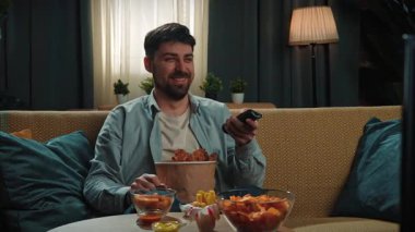 Abur cubur reklamı konsepti. Sakallı adam evde fast food dağıtımı ile vakit geçiriyor, kanepede oturup televizyonda komik filmler izliyor, gülümsüyor ve soslu kızarmış tavuk yiyor. Yavaş çekim