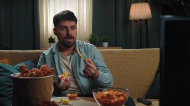 Abur cubur reklamı konsepti. Sakallı adam evde fast food dağıtımı ile vakit geçiriyor, kanepede oturup TV 'de film izliyor, gülümsüyor ve soslu kızarmış patates yiyor. Yavaş çekim