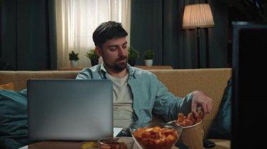 Abur cubur reklamı konsepti. Sakallı adam evde fast food dağıtımı ile vakit geçiriyor, kanepede oturup dizüstü bilgisayar izliyor ve kovadan kızarmış tavuk yiyor. Yavaş çekim