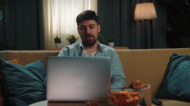 Abur cubur reklamı konsepti. Sakallı adam evde fast food dağıtımı ile vakit geçiriyor, kanepeye oturup bilgisayardan video görüşmesi yapıyor ve soslu kızarmış patates yiyor. Yavaş çekim