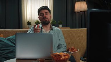 Abur cubur reklamı konsepti. Sakallı adam evde fast food dağıtımı ile vakit geçiriyor, kanepeye oturup bilgisayardan video görüşmesi yapıyor ve soslu kızarmış patates yiyor. Yavaş çekim