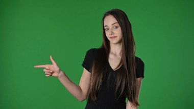 Gençlik duyguları konsepti. Genç kız kameraya poz veriyor gülümsüyor ve parmağıyla işaret ediyor, pozitif ifade, krom anahtar yeşil ekran arka plan modelinde izole edilmiş..