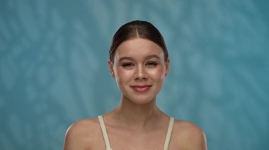 Güzellik konsepti. Stüdyoda makyajlı genç bir kadın, neşeli bir şekilde gülümsüyor, taze pozitif bir ifade, mavi arka planda soyutlanmış. Yavaş çekim.