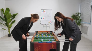 İş kıyafeti giymiş iki kadın, modern ofis ortamında langırt oynamaktan zevk alıyor, iş ve eğlenceyi birleştiriyor..