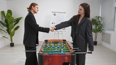 Resmi giyinmiş iki iş kadını arka planda bir strateji tahtası olan langırt masasını devrettiler..