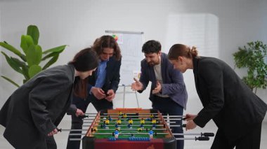 Bir grup meslektaş hevesle masa futbolu oynuyor, takım çalışmasını teşvik ediyor ve ofis ortamında rekabetçi bir ruh yaratıyorlar..