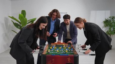 Resmi giyinmiş bir grup iş arkadaşı modern bir ofis alanında eğlenceli bir langırt oyununun keyfini çıkararak takım çalışmasını ve rahatlamayı teşvik ediyor..