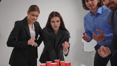 Bir grup profesyonel, kırmızı bardaklarla ofis ortamında takım oluşturma oyununu kazanmaya odaklanmış durumda..