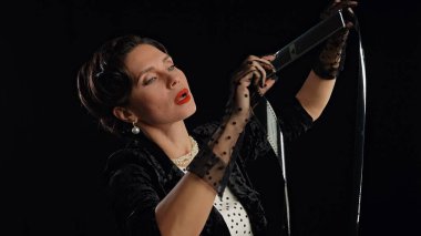 Stüdyoda profesyonel model. Siyah arka planda izole edilmiş fotoğraf makinesine poz veren eski moda saç stili ve makyajlı kadın oyuncu, film makarasından bakan kadın..