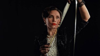 Stüdyoda profesyonel model. Siyah arka planda izole edilmiş fotoğraf makinesine poz veren eski moda saç stili ve makyajlı kadın oyuncu, film makarasından bakan kadın..