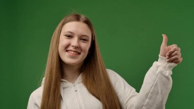 Gençlik duyguları konsepti. Kameraya gülümseyen ve başparmağını jest gibi gösteren genç bir kız, pozitif ifade, krom anahtar yeşil ekran arka plan modelinde izole edilmiş. Yavaş çekim