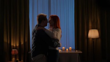Mumlarla çevrili, kucaklaşan ve dans eden bir çiftin romantik bir ortam yarattığı sıcak bir oda. Yavaş çekim.