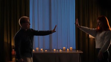 Karanlık bir odada mumlarla neşeyle dans eden genç bir çift. Ağır çekim. Mavi ışıklı pencereye karşı sıcak bir ışıkla romantik bir akşam. Yavaş çekim.