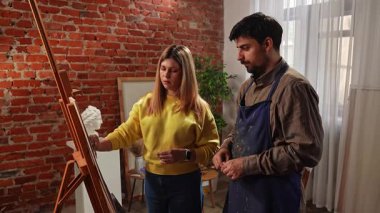 Sanatsal beceriler geliştirmek için eğitim boş zamanı aktivitesi. Şövaledeki yetişkin insanlar antika kadın heykeli çiziyor, önlüklü öğretmen kadın öğrenciye detayları anlatıyor. Yavaş çekim.