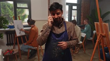 Sanatsal beceriler geliştirmek için eğitim boş zamanı aktivitesi. Yetişkin bir grup insan sehpada oturup antik model kadın heykelinin resimlerini çiziyor. Önlüklü bir öğretmen akıllı telefondan konuşuyor. Yavaş çekim.