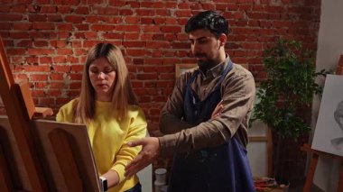 Sanatsal beceriler geliştirmek için eğitim boş zamanı aktivitesi. Şövaledeki yetişkin insanlar antika kadın heykeli çiziyor, önlüklü öğretmen kadın öğrenciye detayları anlatıyor. Yavaş çekim.