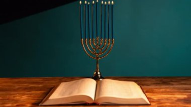 Güzel aydınlatılmış bir menorah ve kırsal bir ahşap masaya karşı açık bir kitap. Sıcak parıltı, Hanuka bayramında gelenek ve inancı simgeliyor..