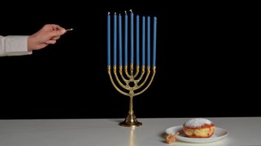 El, Hanuka geleneklerini sembolize eden güzel bir menoranın üzerine mavi bir mum yakar. Yakınlarda bir tabak sufganiyah oturuyor ve bu kutsal bayramın şenlikli atmosferini arttırıyor..