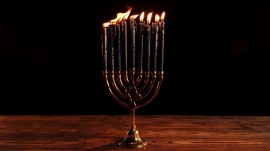 Çok güzel işlenmiş bir bronz menorah ahşap bir masada görkemli bir şekilde duruyor, mumları usulca parlıyor..