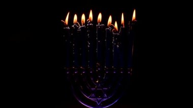 Çok güzel aydınlatılmış bir menorah, koyu bir arka planda gururla durur, mumları sıcacık parlar. Bu kutsal ayin Hannuka 'nın neşesini sembolize eder. İnancın ve kültürün şenlikli bir kutlaması..