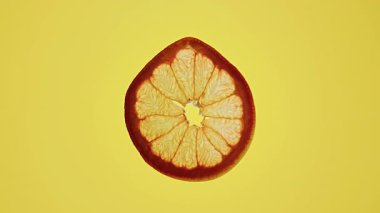 Canlı sarı bir zemin üzerinde ışık, gösterişli doku ve renk kontrastıyla aydınlatılmış turuncu bir dilimin yakın plan görüntüsü.