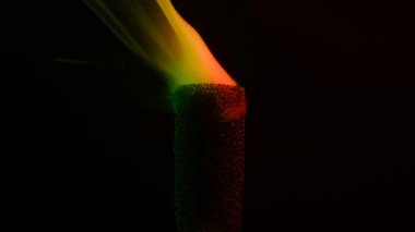 Arkaplanda yanan tütsüden kıvrılan canlı yeşil ve turuncu dumanların sanatsal bir gösterisi. Yavaş çekim