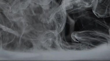 Ölümcül beyaz duman zerafetle karanlık bir arkaplanda kıvrılarak karmaşık soyut desenler oluşturur. Yavaş çekim