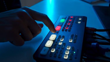 Profesyonel bir ses karıştırıcı çalıştıran bir elin yakın plan görüntüsü, ses yönetimi için kontrol düğmeleri ve arayüzü vurgulanıyor.