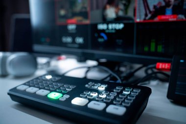 Arka planda içeriği gösteren bir monitörle modern bir video prodüksiyon kontrol panelinin ayrıntılı bir görüntüsü.