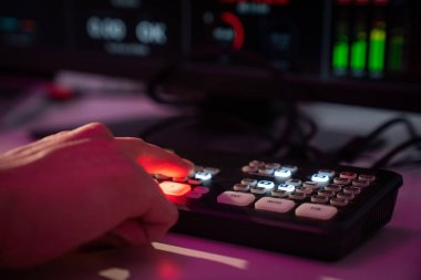 Profesyonel bir yayın ortamında, aydınlatılmış düğmelerin yer aldığı bir video değiştirici kullanan bir elin yakın çekimi.