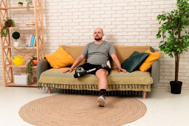 Günlük hayat ve engelli insanların hayatı. Biyonik protez bacak sakatlığı olan bir adam evdeki kanepede oturup protez bacağı dizine kadar bükülmüş şekilde dinleniyor..