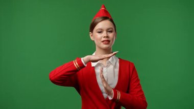 Uçuş ekibi reklam konsepti. Hostes kılığındaki kadın kırmızı üniformalı el hareketi işareti gösteriyor. Renkli yeşil ekran stüdyo arka planında izole edilmiş..