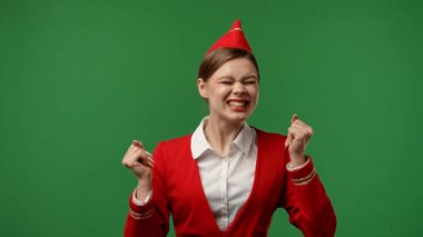 Uçuş ekibi reklam konsepti. Hostes gibi giyinmiş, kırmızı üniformalı bir kadın mutluluktan uçuyor ve dans ederek kazanıyor. Krom renkli yeşil perde stüdyo arka planında izole edilmiş..