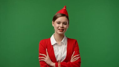 Uçuş ekibi reklam konsepti. Kırmızı üniformalı hostes kılığındaki kadın çapraz kollarıyla poz veriyor ve gülümsüyor. Renkli yeşil ekran stüdyo arka planında izole edilmiş..