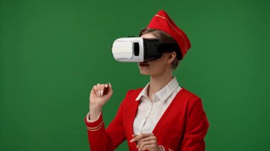 Uçuş ekibi servis ilanı. Hostes kılığındaki kırmızı üniformalı bir kadın sanal menü kullanarak krom anahtar yeşil ekran stüdyo arka planında izole edilmiş VR gözlükler takıyor ve kaydırıyor..