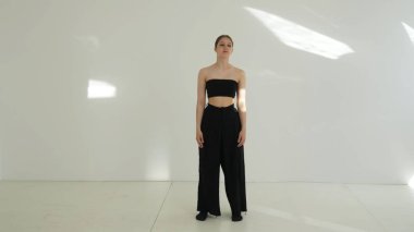 Siyah elbiseli genç kadın beyaz arka planda çağdaş dans ediyor..