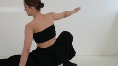 Siyah elbiseli genç kadın beyaz arka planda çağdaş dans ediyor..