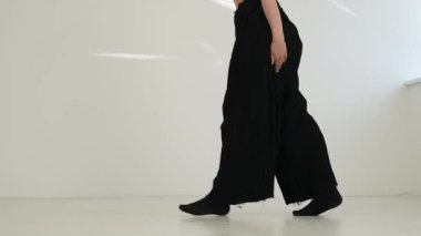 Siyah elbiseli genç kadın beyaz arka planda çağdaş dans ediyor..