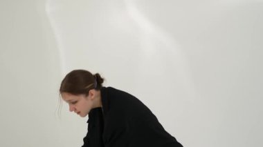 Siyah elbiseli genç kadın beyaz arka planda çağdaş dans ediyor..