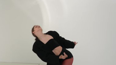 Siyah elbiseli genç kadın beyaz arka planda çağdaş dans ediyor..