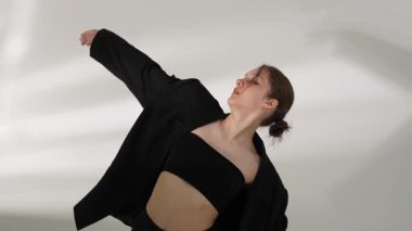 Siyah elbiseli genç kadın beyaz arka planda çağdaş dans ediyor..