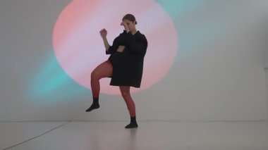 Siyah elbiseli genç kadın neon arka planda çağdaş dans ediyor..