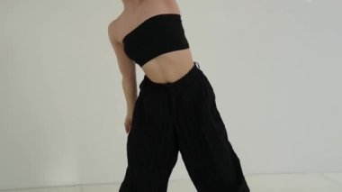 Siyah elbiseli genç kadın beyaz arka planda çağdaş dans ediyor..