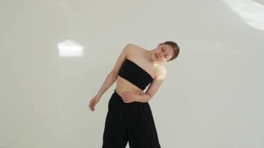Siyah elbiseli genç kadın beyaz arka planda çağdaş dans ediyor..