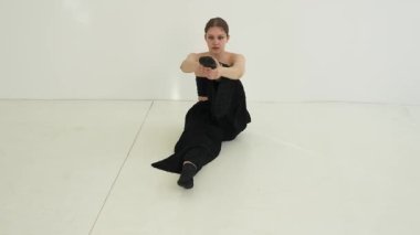 Siyah elbiseli genç kadın beyaz arka planda çağdaş dans ediyor..