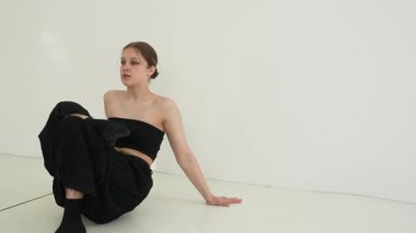 Siyah elbiseli genç kadın beyaz arka planda çağdaş dans ediyor..