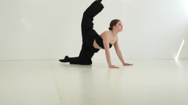 Siyah elbiseli genç kadın beyaz arka planda çağdaş dans ediyor..